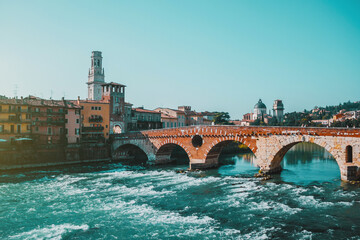 Obraz premium Sunny day in old city Verona, Italy. Rough river embankment, arch bridge, waves and landmarks. Vacation in Europe. Historical buildings.
