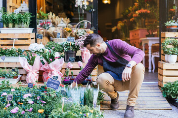 Flower store owner squatting down putting up the plants in the window.