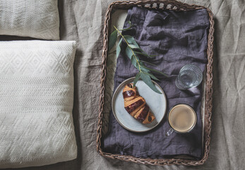 Wicker tray with coffee and croissant on a linen bed. Breakfast in bed