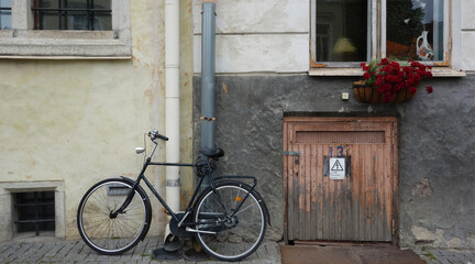 Fototapeta na wymiar a bicycle on the sidewalk under a window with red flowers, Tallinn, Estonia