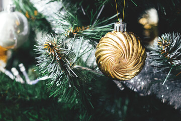 Spiral vortex golden ball on artificial Christmas tree with silver tinsel garland. Selective focus....