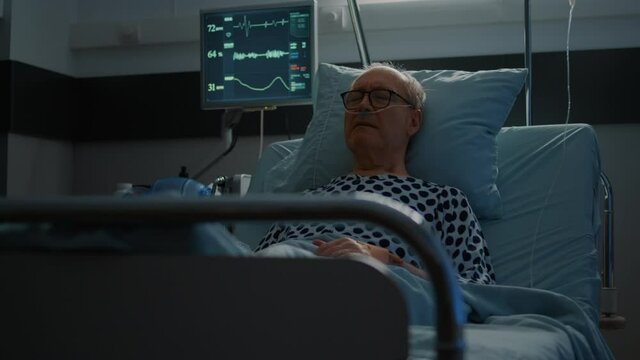Sick elderly man with health problems staying in hospital ward bed prepared for medical treatment. Patient with nasal oxygen tube and oximeter waiting to cure heavy illness, disease.