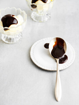 Hot Fudge Sundaes In Background With Messy Hot Fudge Spoon In The Forground. Bright And Sunny On A Metal Surface.