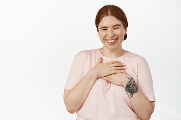 Image of carefree young woman with red combed hair and freckles, holding hands on chest, laughing sincere and smiling white teeth, positive emotions and face expression, white background