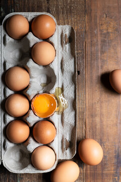 Chicken eggs in a cardboard carton with one cracked egg.