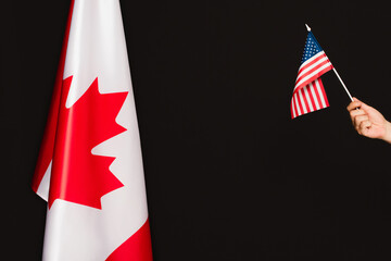 cropped view of man holding american flag near canadian symbol isolated on black