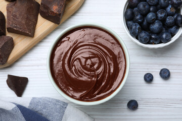Delicious chocolate cream and blueberries on white wooden table, flat lay