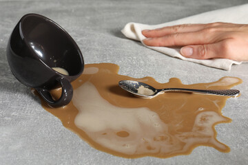 Woman wiping spilled coffee on grey table, closeup - obrazy, fototapety, plakaty