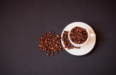 Coffee cup with roasted coffee beans on dark background.