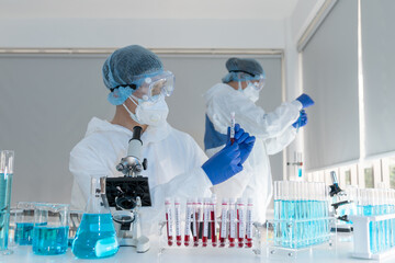 Asian scientist in laboratory holding a covid-19 infected blood tube. Virologists research and...