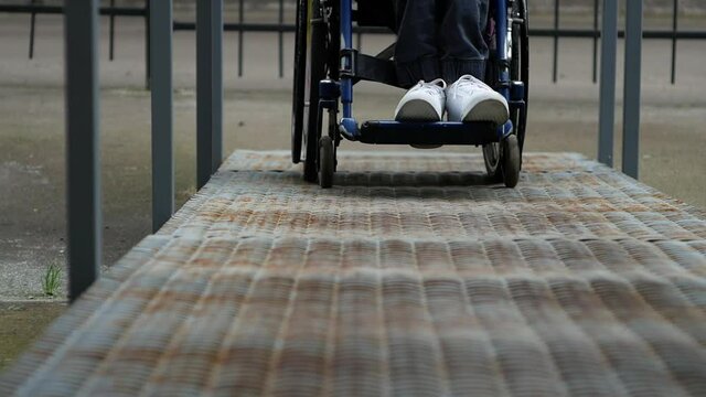 A disabled young man in a wheelchair drives into the ramp. Close up of wheelchair wheel and disabled person's legs.