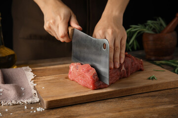 Woman cutting fresh raw meat at wooden table, closeup