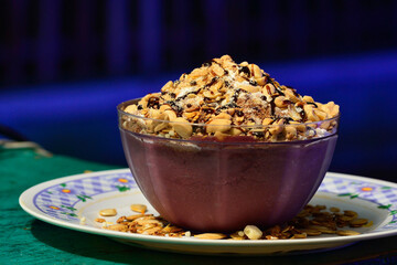 Acai cream with granola and peanuts in glass bowl.