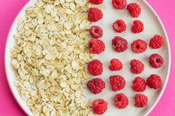 Ripe raspberry fruits with oatmeal flakes on plate, healthy pile of summer berries top view. Healthy proper breakfast concept with free copy space for text