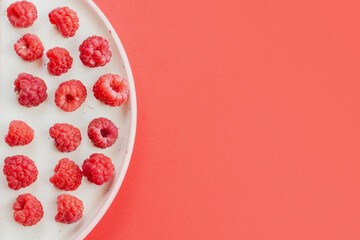 Ripe raspberry fruits on plate, healthy pile of summer berries  top view. Pattern flat lay of red scarlet  raspberry on pink background with free copy space for text