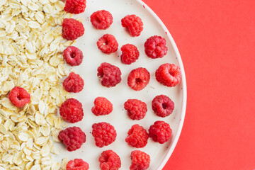 Ripe raspberry fruits with oatmeal flakes on plate, healthy pile of summer berries top view. Healthy proper breakfast concept with free copy space for text