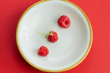 Ripe organic raspberry berry on plate, healthy pile of summer berries  top view. Pattern flat lay of scarlet  raspberry on red background