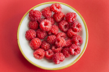 Ripe organic raspberry berry on plate, healthy pile of summer berries  top view. Pattern flat lay of scarlet  raspberry on red background