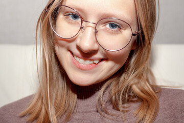 Portrait of a young teenage girl with glasses. Girl smiles and shows crooked growing teeth. You need to go to the dentist to install braces.