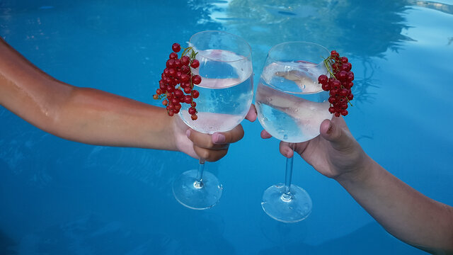 the hands of a man and a woman are holding glasses with a non-alcoholic refreshing summer cocktail on the background of the blue water of the pool. - Powered by Adobe