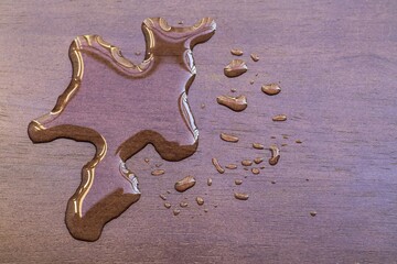 Water spilled on the dark brown wood surface of plywood table.