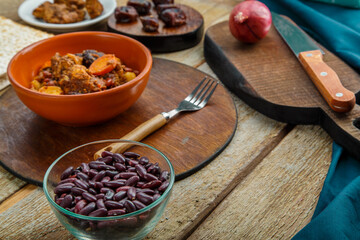 Jewish dish chelnt with meat in a plate on a wooden table on a stand next to ingredients.