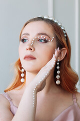 close-up portrait of a red-haired, young woman with makeup made of pearls in the form of a zigzag...