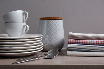 Stack of soft kitchen towels and dishware on wooden table against grey background