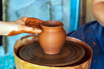 Fototapeta na wymiar Potter makes on the pottery wheel clay pot. Hand of the master close-up during work. Ancient national craft