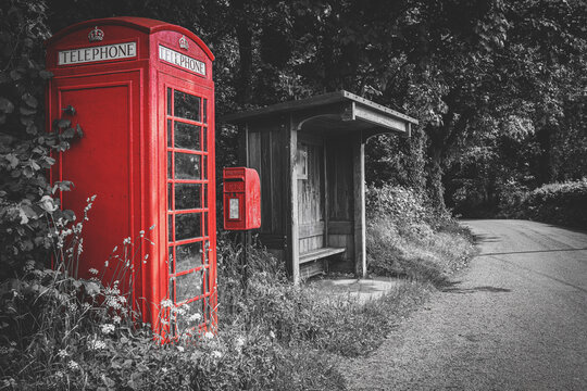 Traditional red British telephone booth, post box and wooden bus stop, selective color on black and white background, no people. Wales, UK