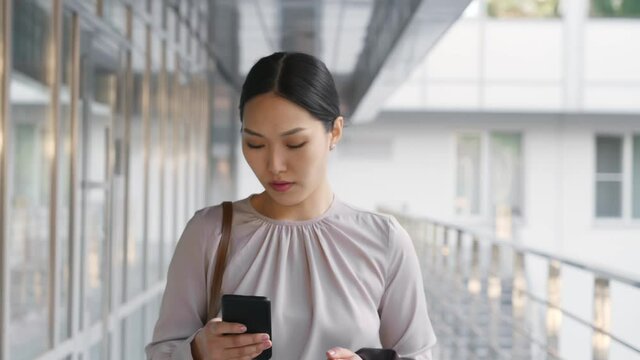 Asian businesswoman commuting to work checking messages on mobile phone outside office building