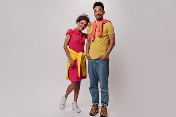 Fototapeta premium Portrait of Woman in red dress and man in jeans and orange T-shirts. Pretty young girl and dark-skinned guy pose on white isolated background