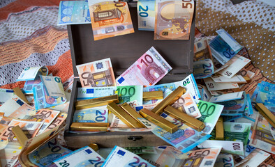 A pile of bills strewn and golden bars scattered across the bed in a wooden chest. A treasure chest full of money. Finance and savings concept.