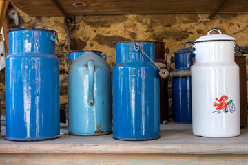 Blue, turquoise and white retro milk containers standing on a wooden shelf. 