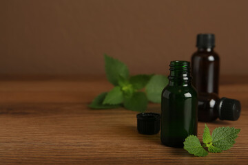 Glass bottles of nettle oil and leaves on wooden table against brown background, space for text