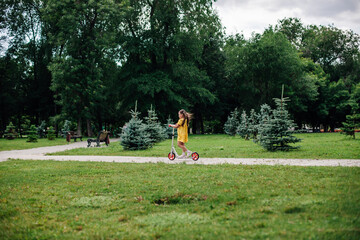 a girl on a scooter, a useful fitness walk through the forest with her family on a summer weekend. 