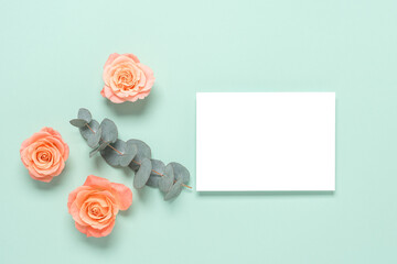 Blank white card mockup with rose flowers and eucalyptus branch on green mint pastel background. Wedding stationery template. Top view, flat lay.