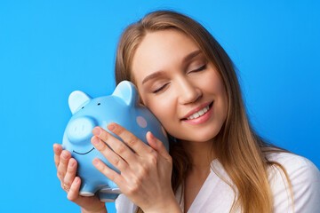 Beautiful smiling young woman with piggy bank on blue background