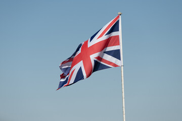 A photograph of the union flag on a mast blowing gently in the wind. Taken against a light blue clear sky