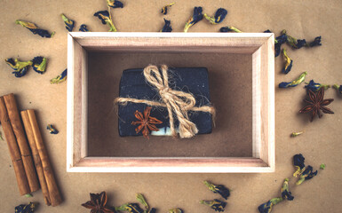 A block of natural carbon soap in a wooden box with cinnamon sticks.