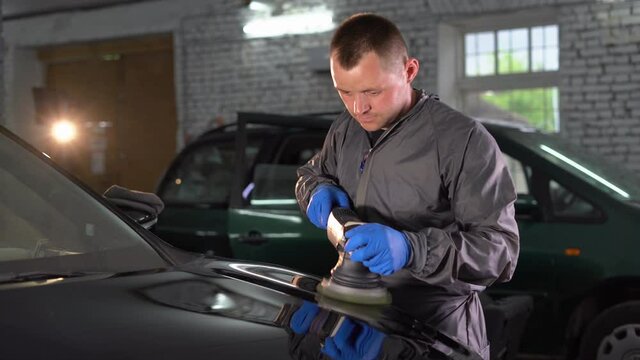 A worker polishes the hood of a car with a special grinder and wax from scratches at a car service. Professional car detailing and service concept.