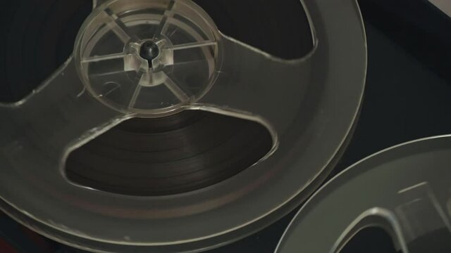 Close up of bobbin. Reel film tape is rotating at a vintage player. Reel to reel tape recorder playing. Popular Disco Trends 60s, 70s, 80s, 90s. Old school concept.