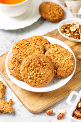 Healthy homemade oatmeal cookies with peanuts in a white plate on a light gray kitchen table closeup	