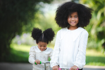 afro-american sibling, brother teaching his younger sister riding scooter on the street, family concept, Kids play outdoors with scooters, Active leisure and outdoor sport for child.