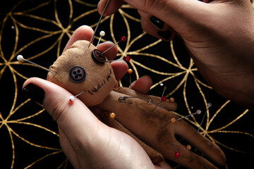 Woman stabbing voodoo doll with needle at table, closeup. Curse ceremony