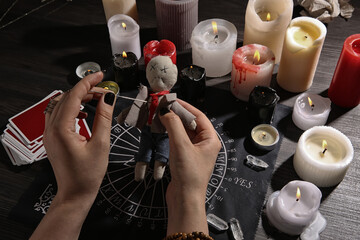 Woman stabbing voodoo doll with needle at table, closeup. Curse ceremony