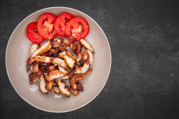 sliced fried pork with tomato in brown ceramic plate on dark tone texture background with copy space for text, top view