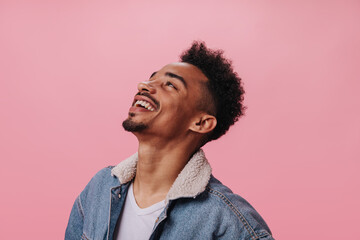 Happy man in denim outfit smiling on pink background. Cheerful brunette guy in white t-shirt laughing on isolated backdrop - obrazy, fototapety, plakaty