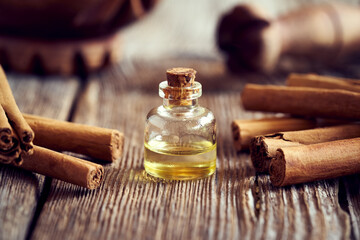 A bottle of aromatherapeutic essential oil with Ceylon cinnamon sticks - obrazy, fototapety, plakaty