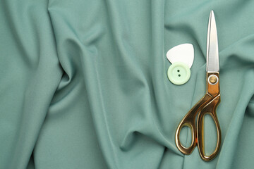 Scissors, button and tailor's chalk on green fabric, flat lay. Space for text